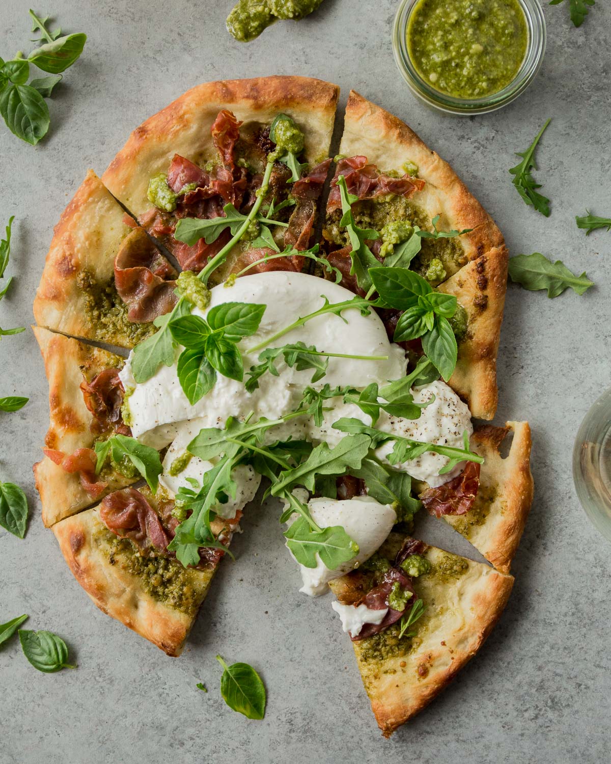 overhead image of a homemade pesto pizza on a grey countertop