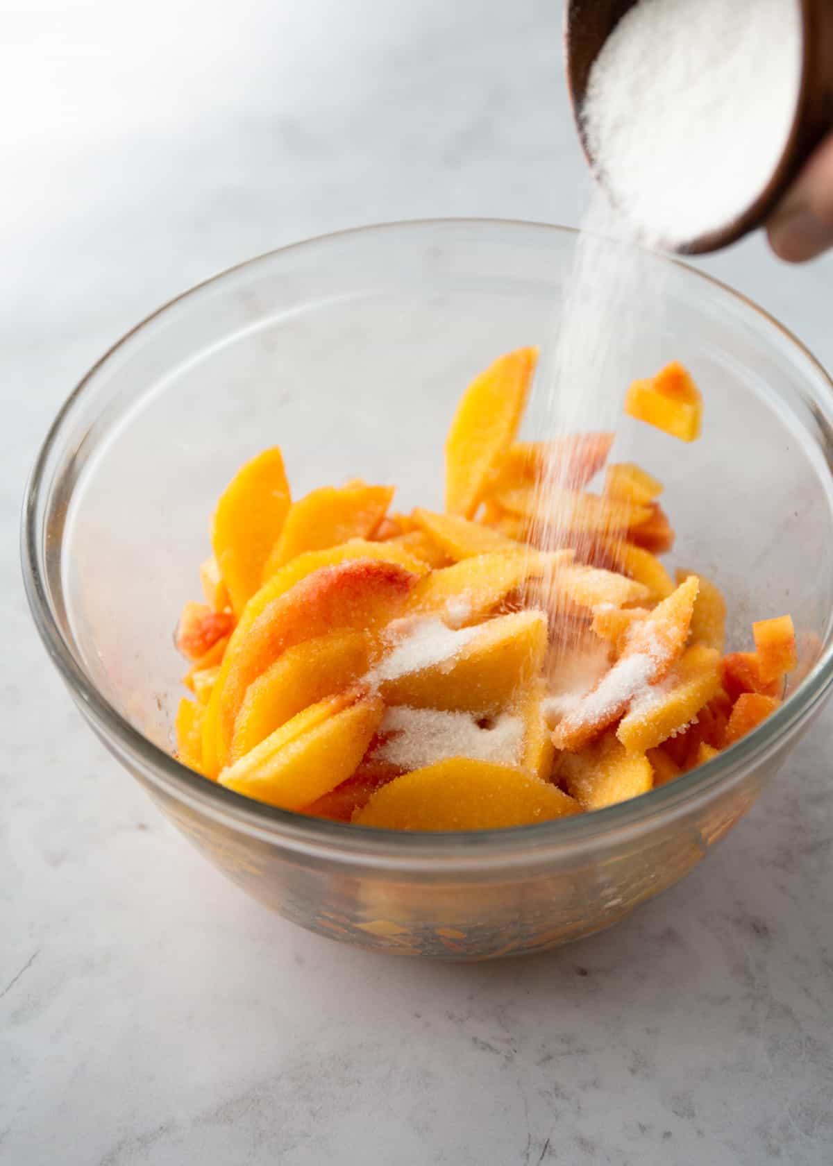 adding cream to sliced peaches in a clear glass bowl