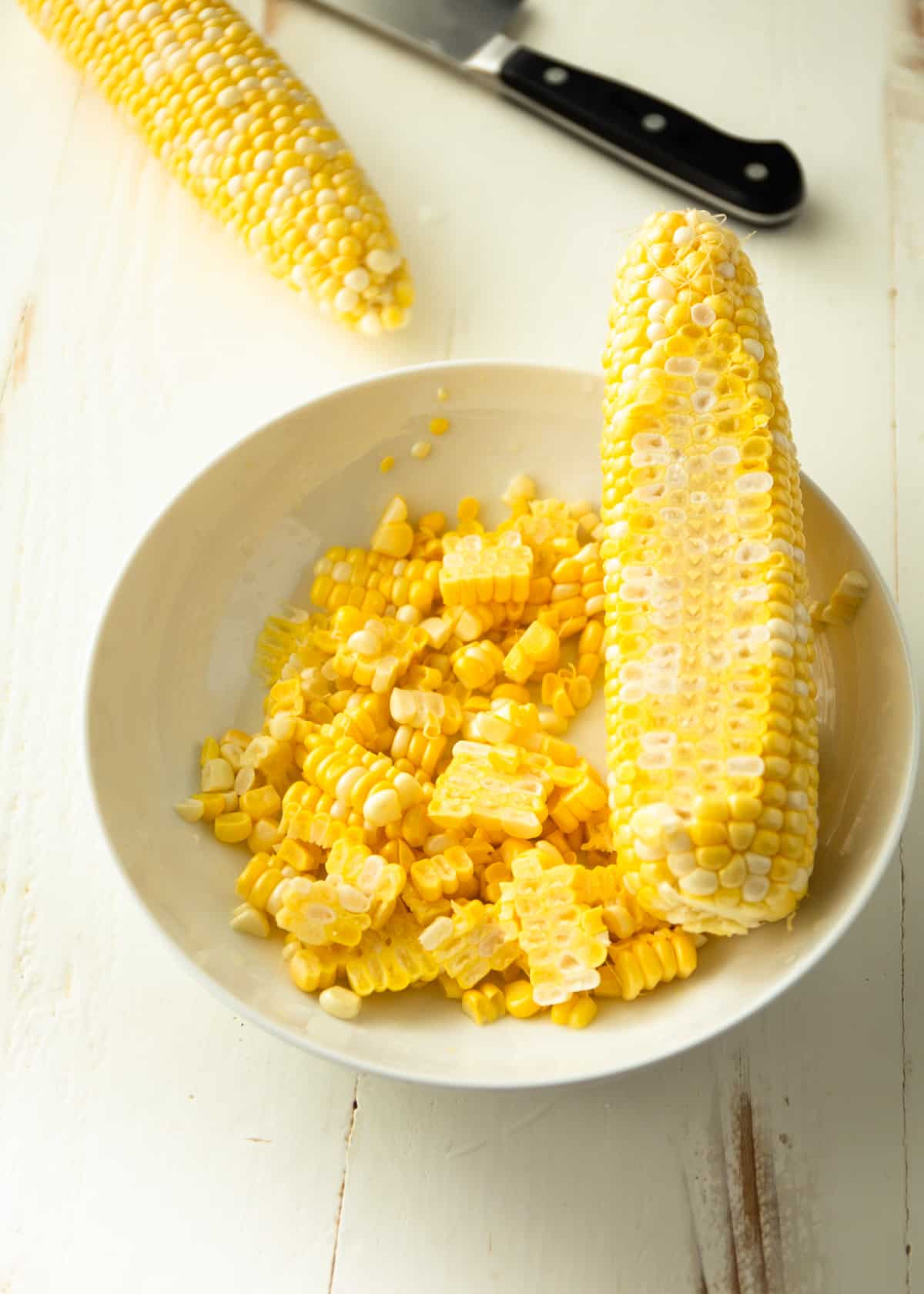 overhead image of cutting corn off the cob into a white bowl