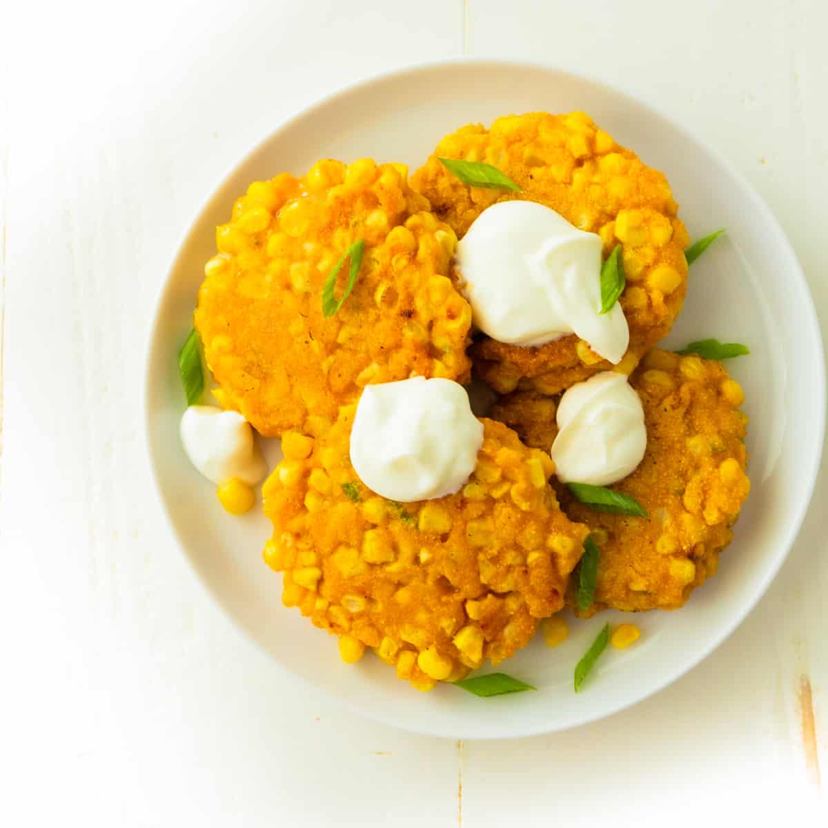 overhead image of corn fritters topped with sour cream on a white plate