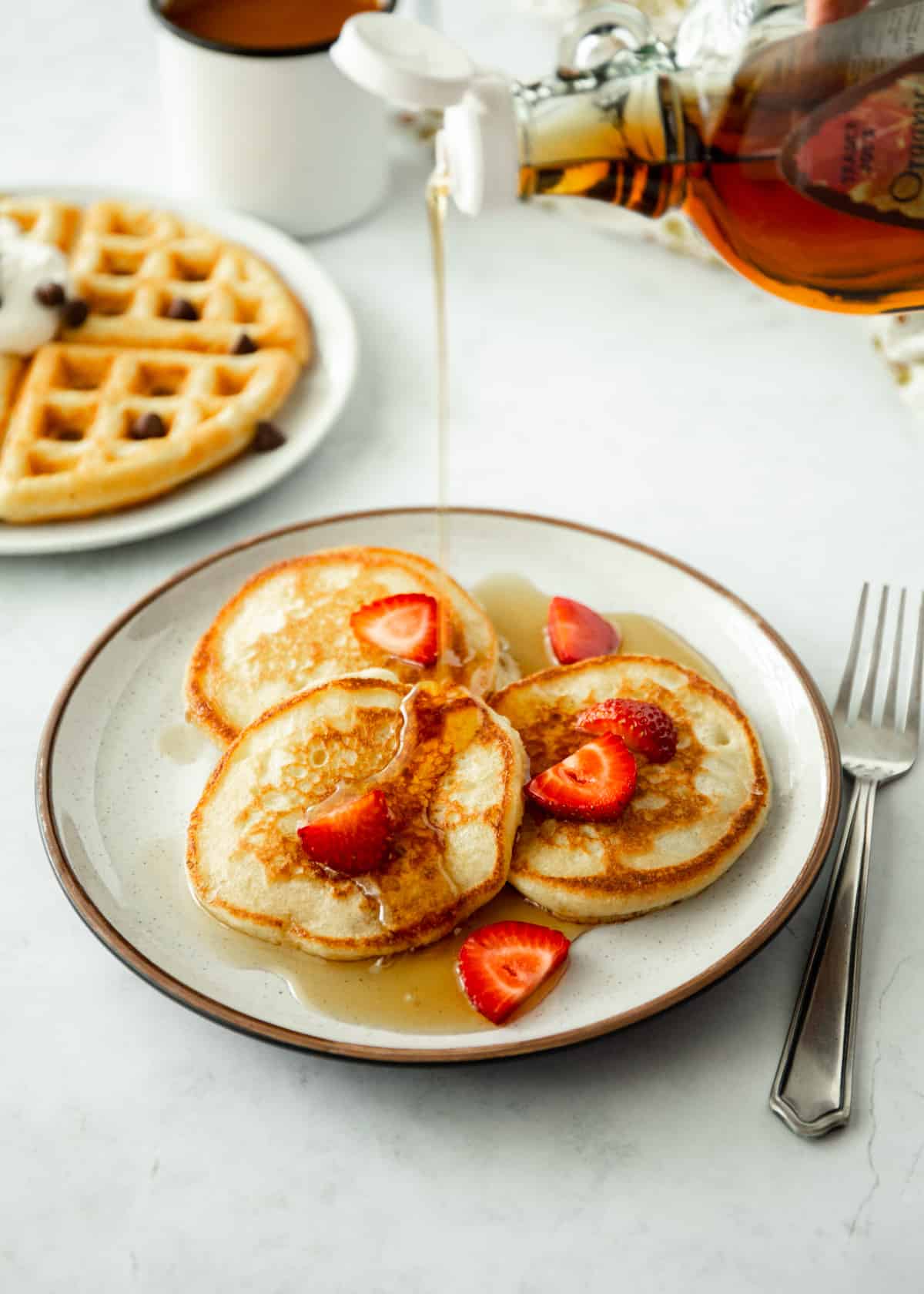 pouring syrup over pancakes with strawberries