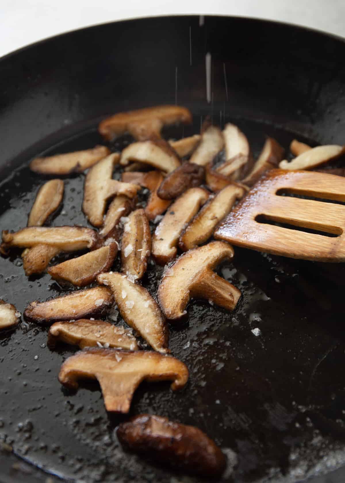 stirring mushrooms in a cast iron skillet