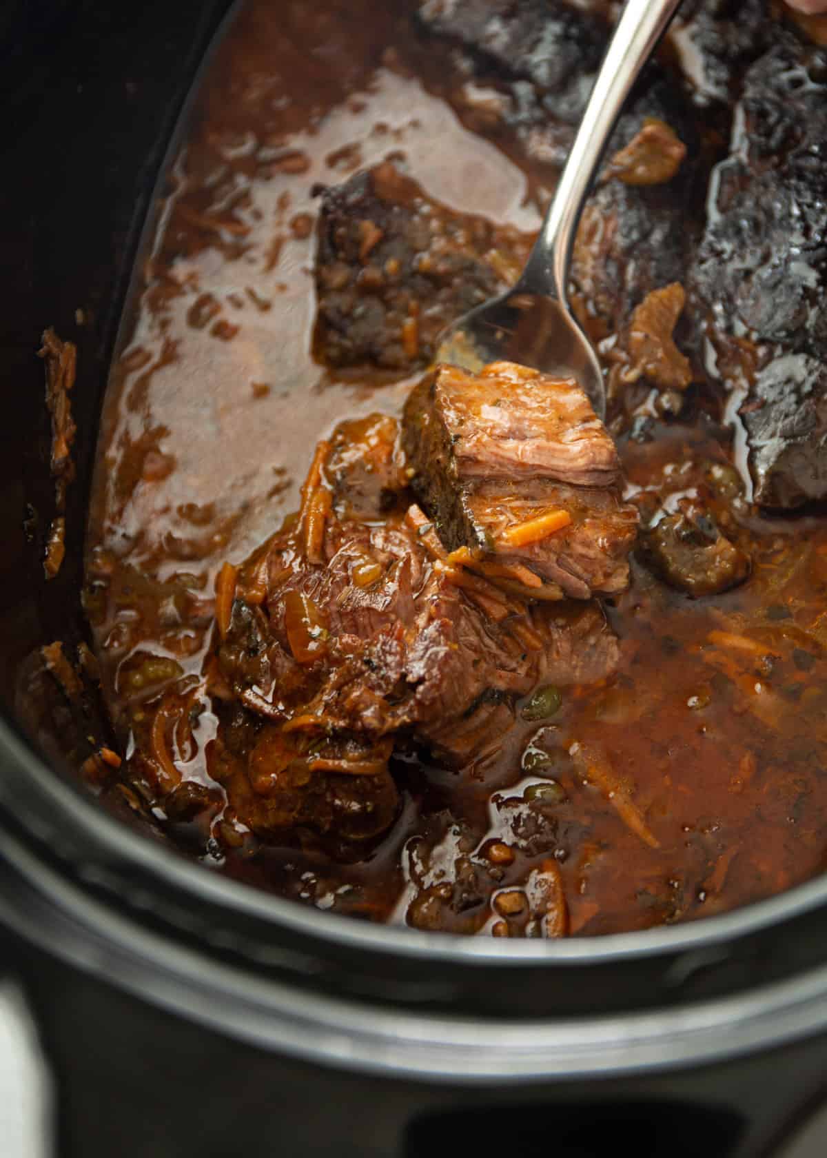 overhead image of a spoon holding roast in a slow cooker