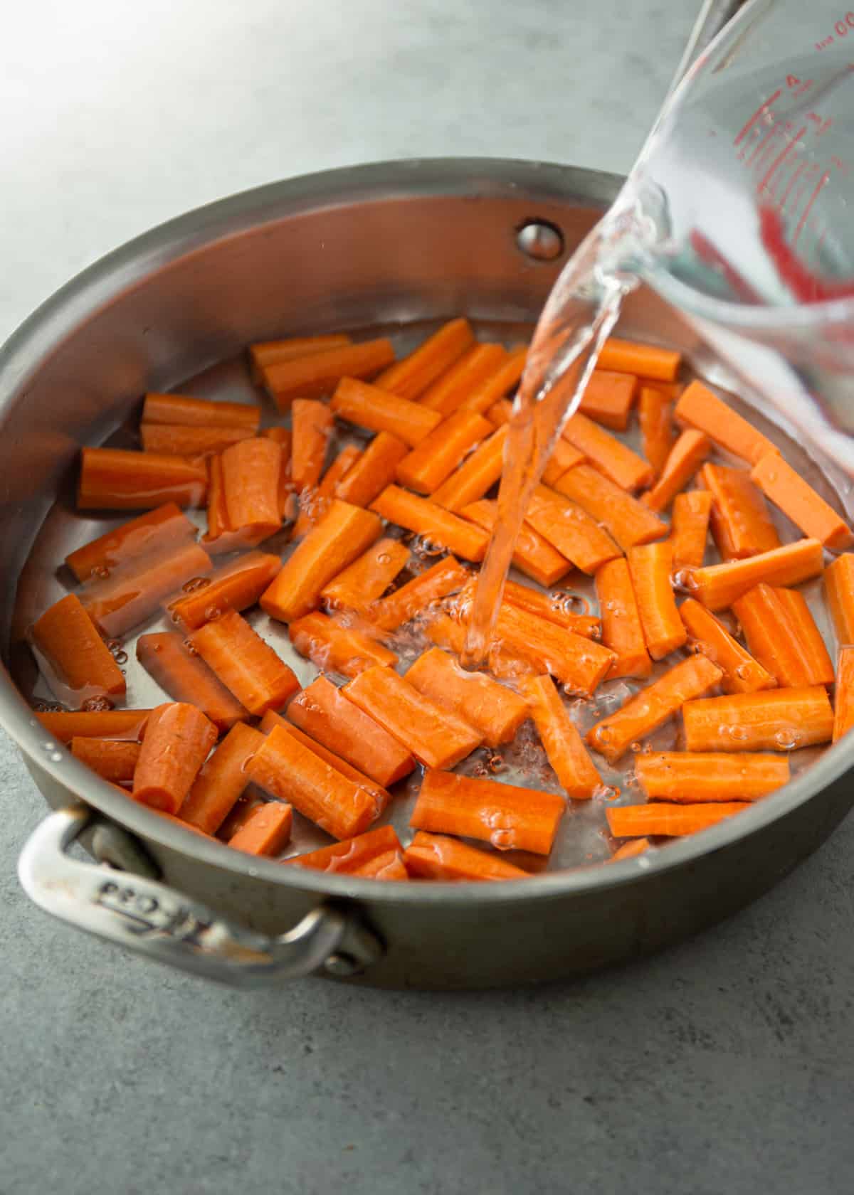 adding water to cut carrots in a saute pan