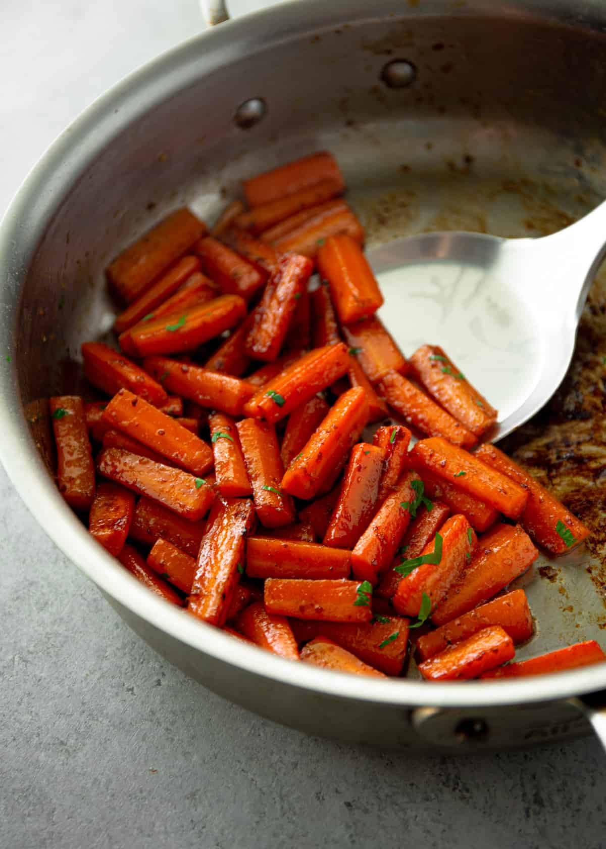 using a spatula to remove cooked carrots from a saute pan