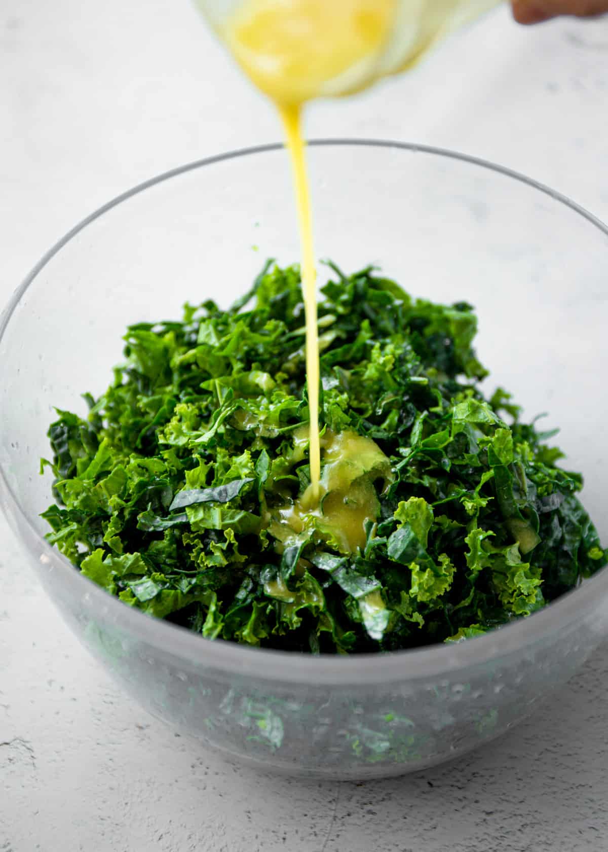 adding dressing to kale in a clear bowl