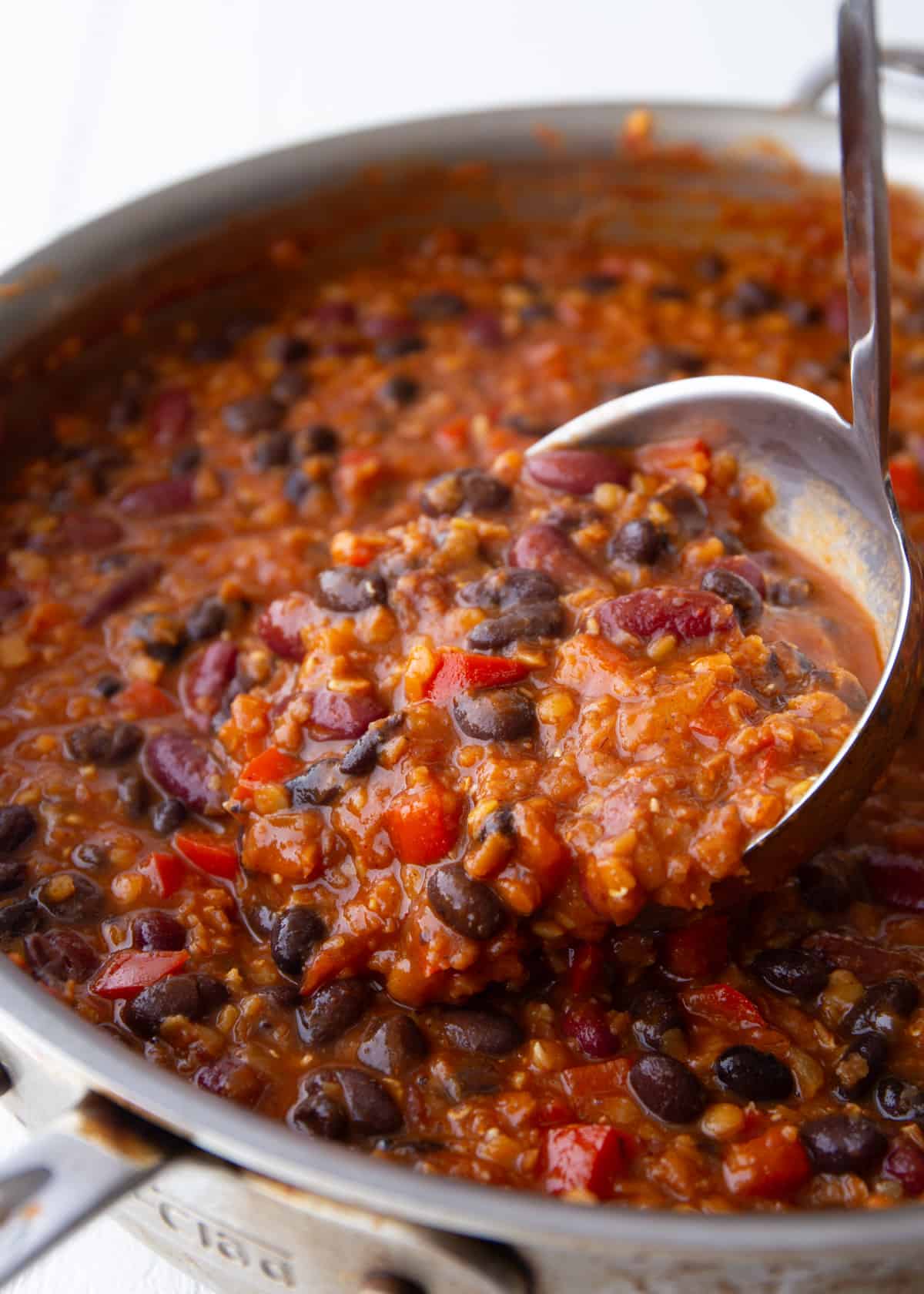 bean and lentil vegetarian chili in a ladle and large saute pan