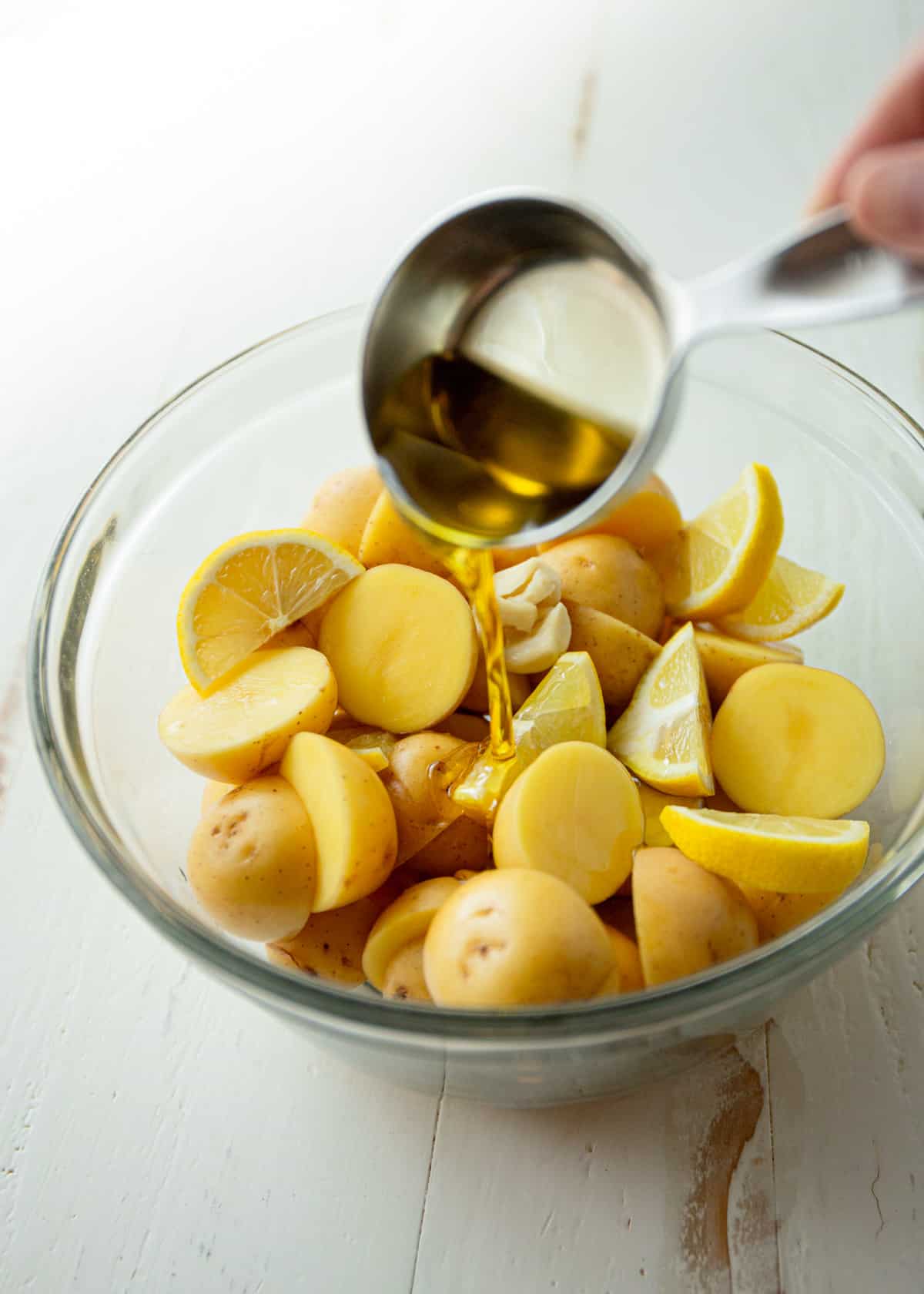 adding oil to cut potatoes and lemon slices in a clear glass bowl