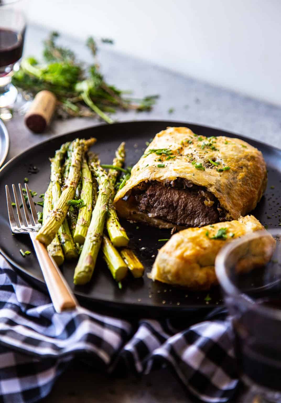 lamb wellington and asparagus on a black plate