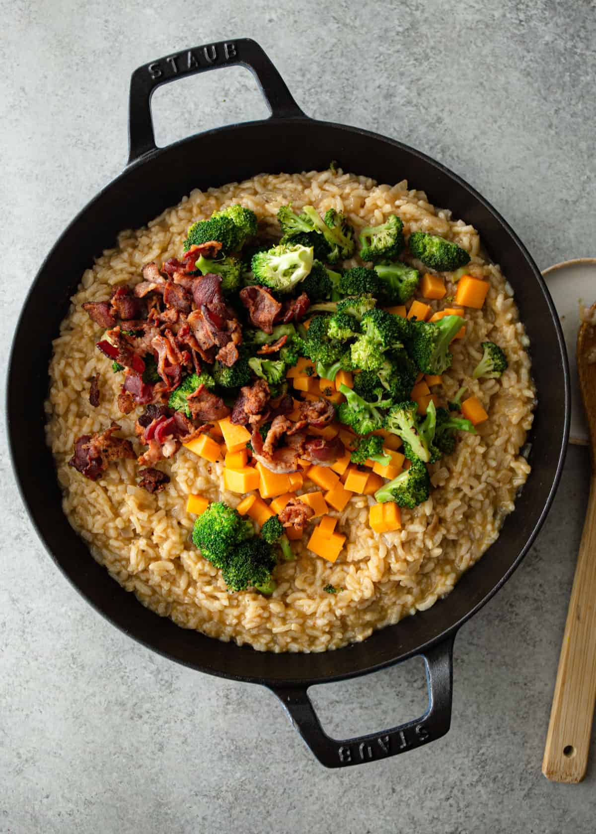 adding broccoli, cheddar and bacon to risotto in a cast iron skillet