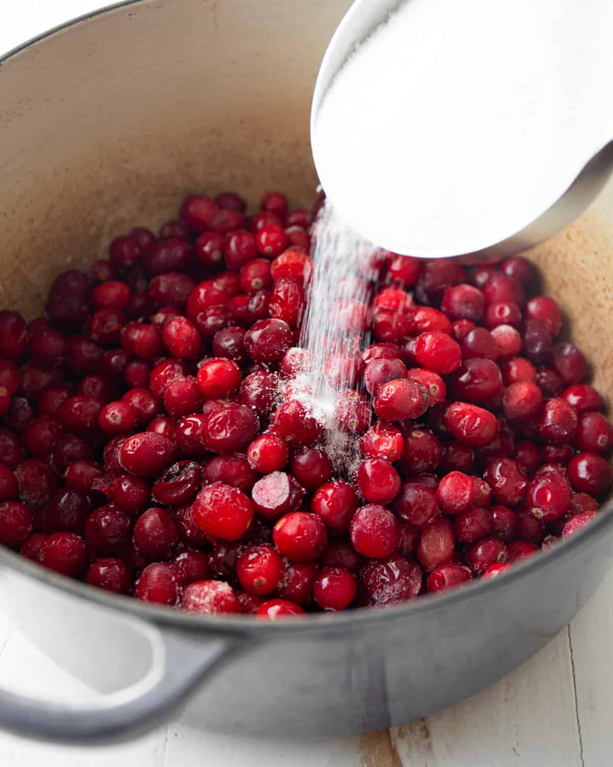 adding sugar to cranberries in a blue dutch oven