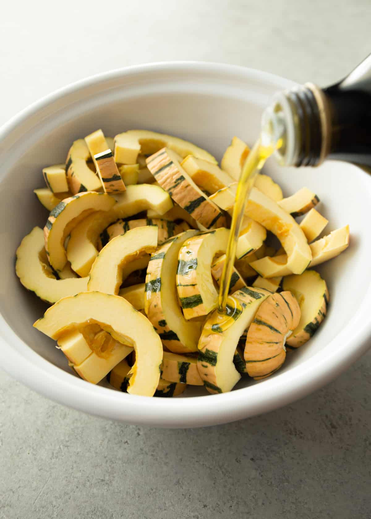 adding oil to sliced squash in a white bowl