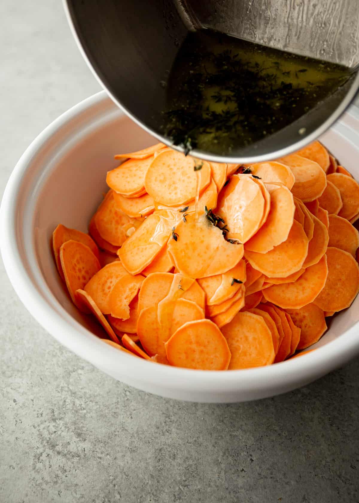 adding butter to sliced sweet potatoes in a white bowl