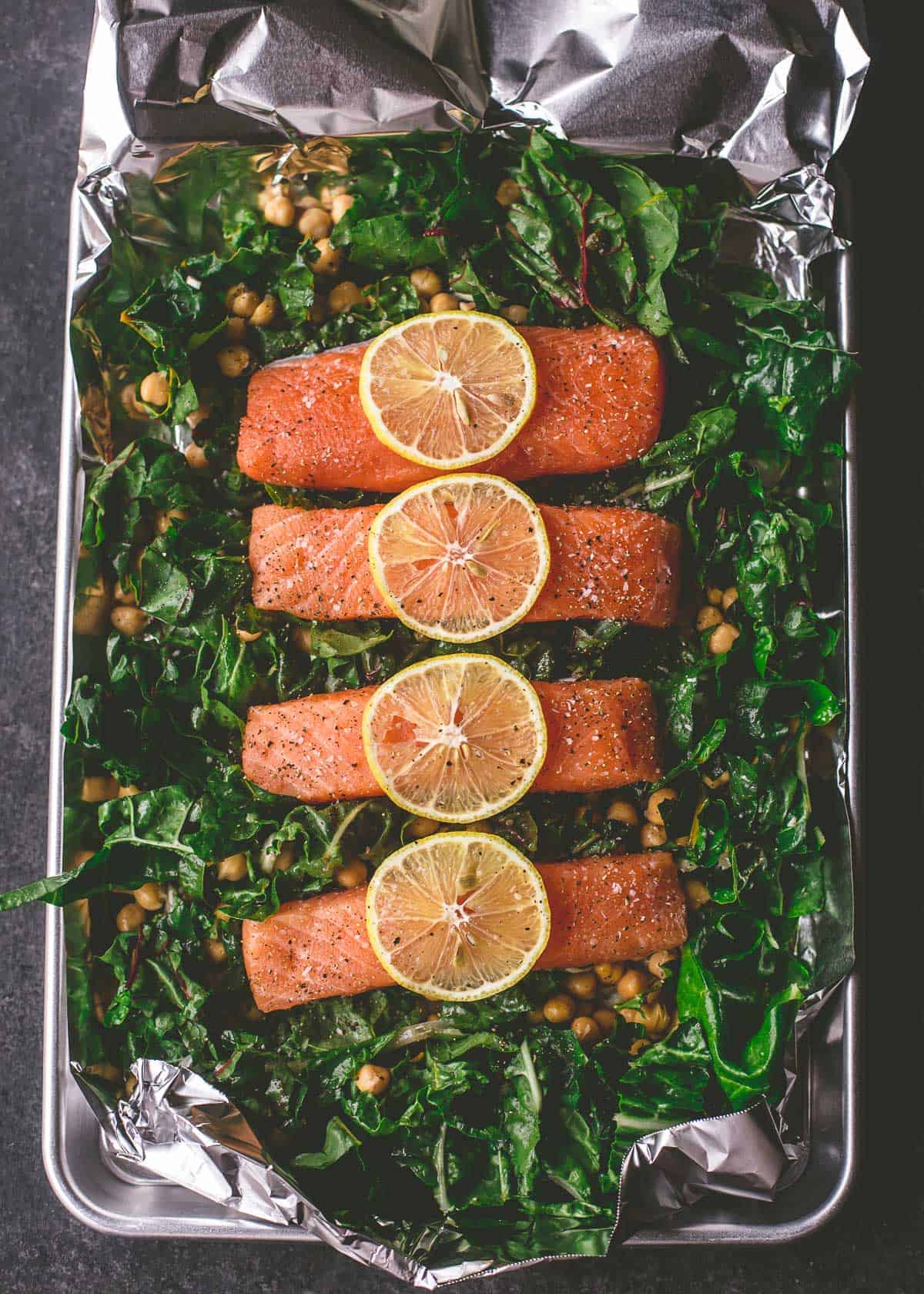 overhead image of salmon filets, greens and chickpeas in a foil wrap