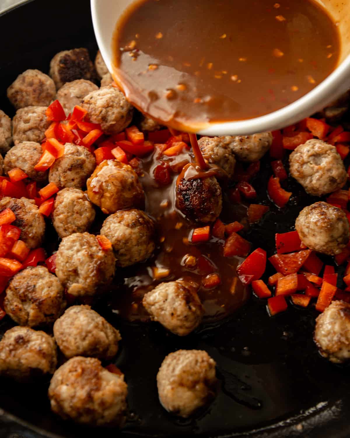 adding kung pao sauce to meatballs in a cast iron skillet