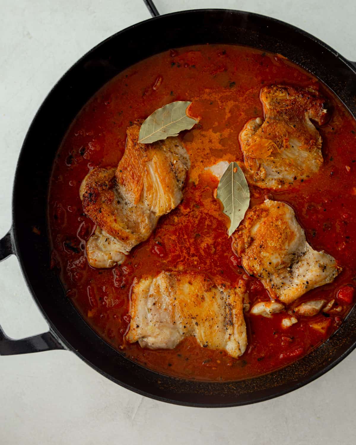 overhead image of chicken and sauce in a black dutch oven