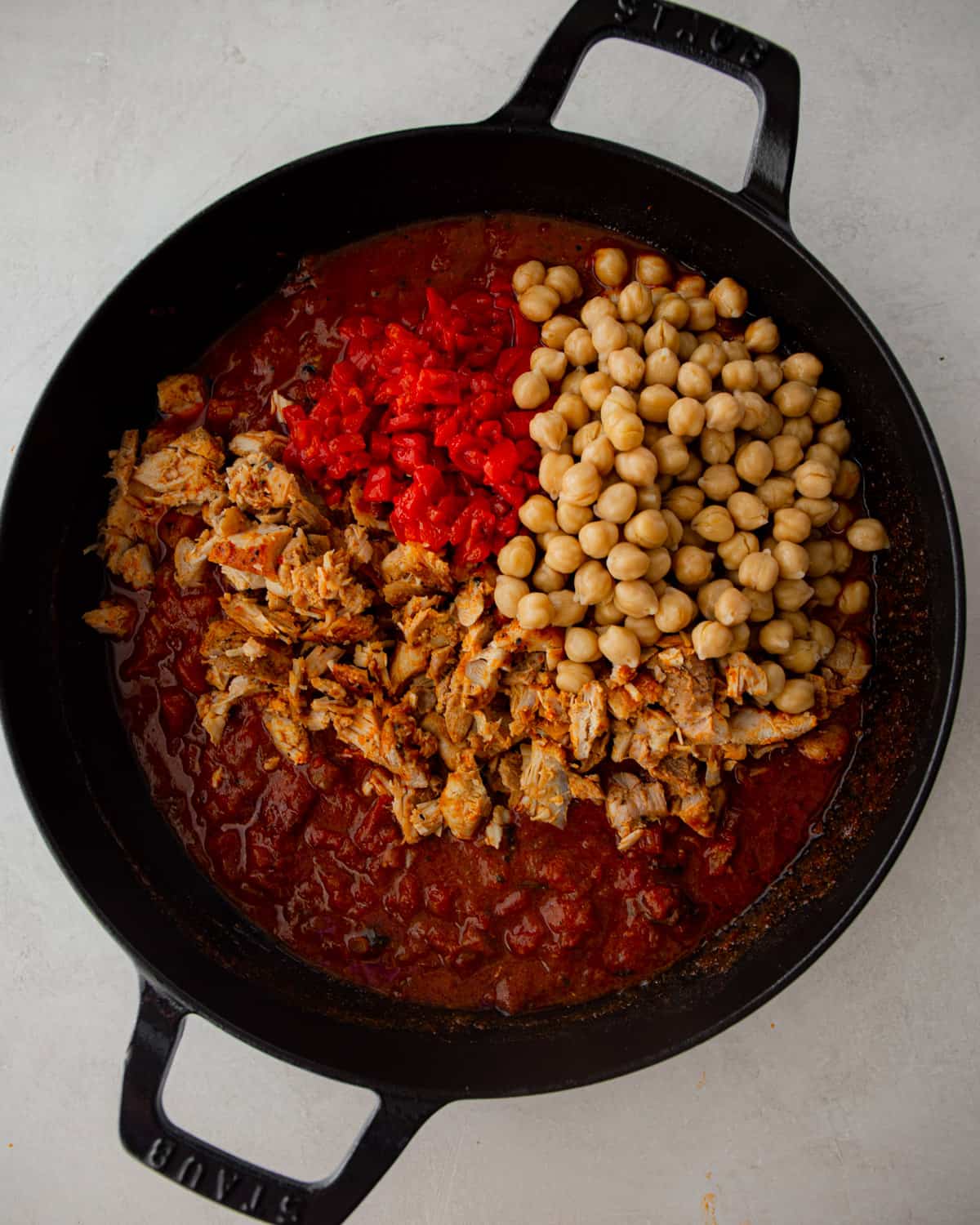 overhead image of chickpeas, chicken and spices in a black dutch oven