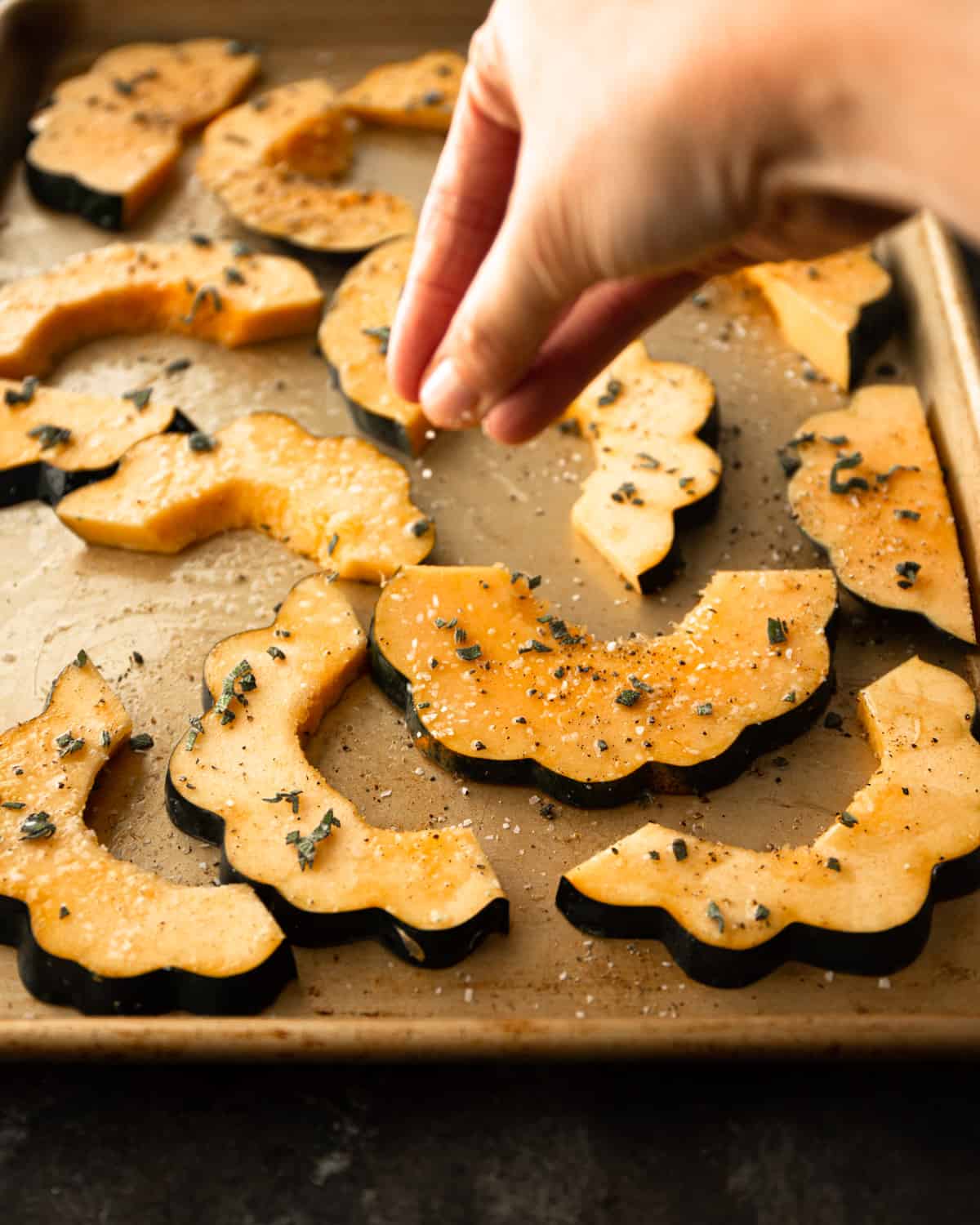 adding seasoning to slices of acorn squash on a sheet pan