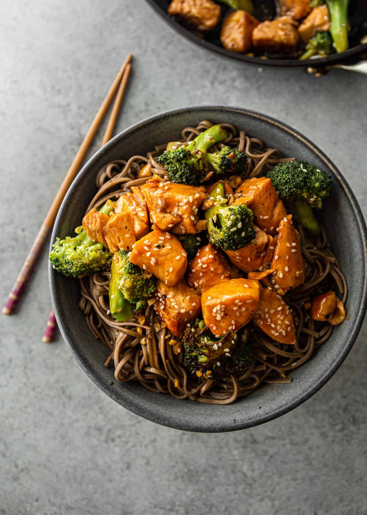 overhead image of teriyaki salmon over noodles with broccoli on a grey plate