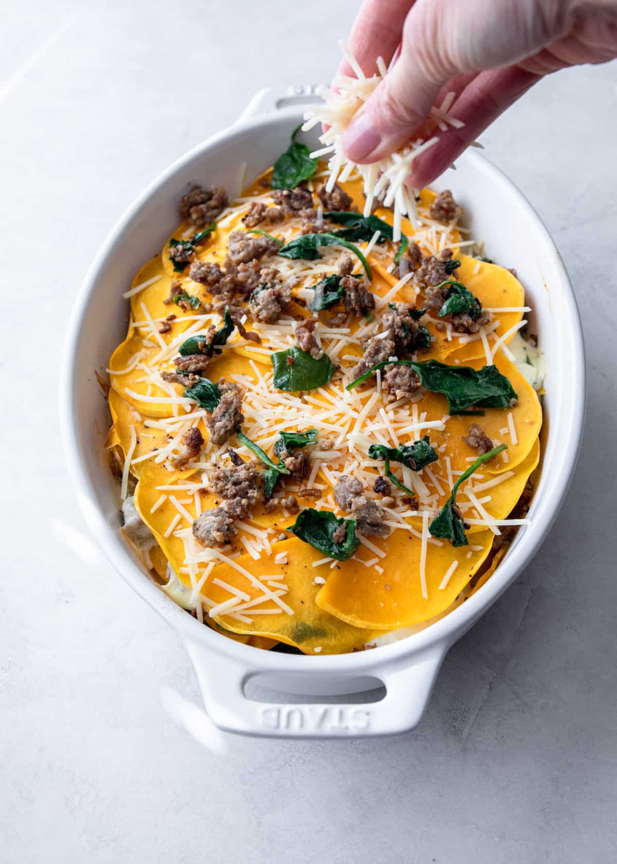 sprinkling cheese on layered lasagna in a white baking dish