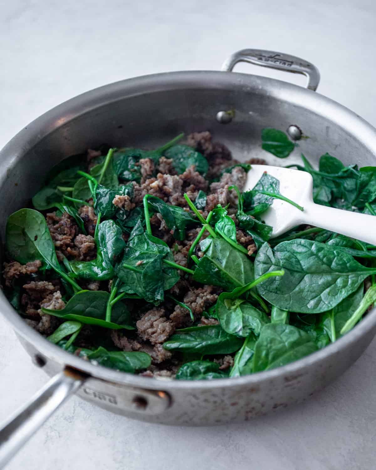 stirring spinach in a skillet with a silicone spatula