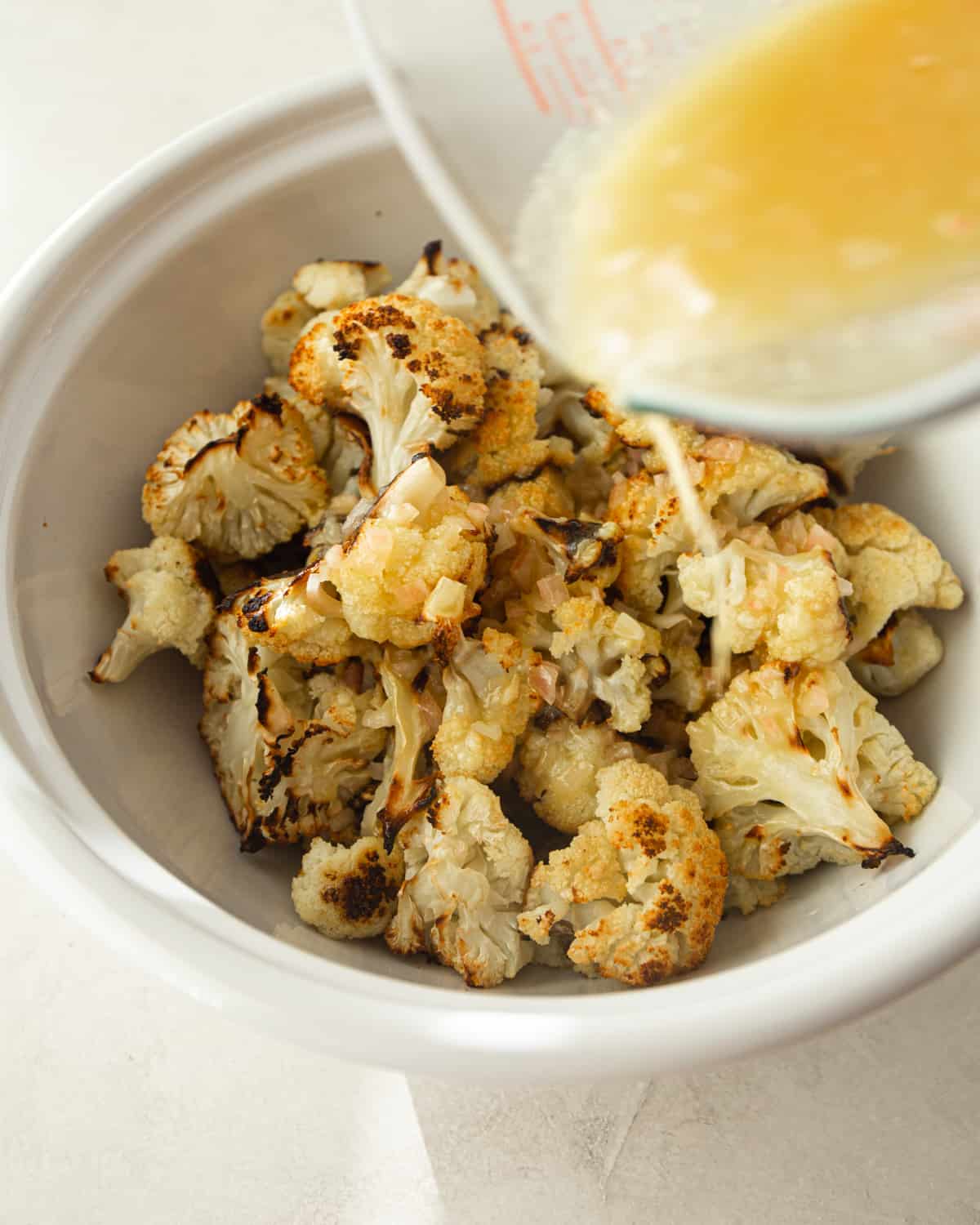 adding vinaigrette to cauliflower in a white bowl