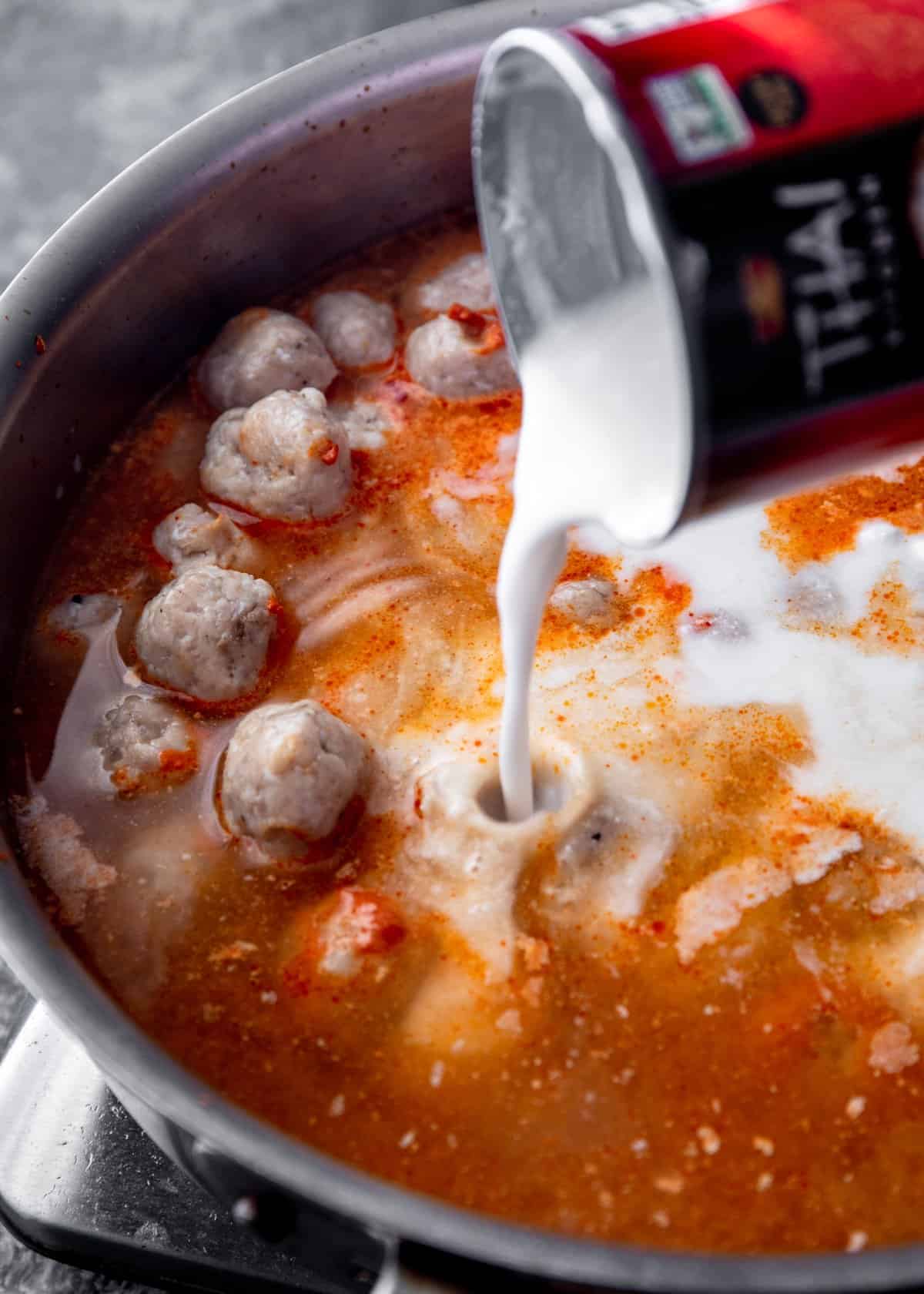 adding coconut milk to curry and meatballs in a saute pan