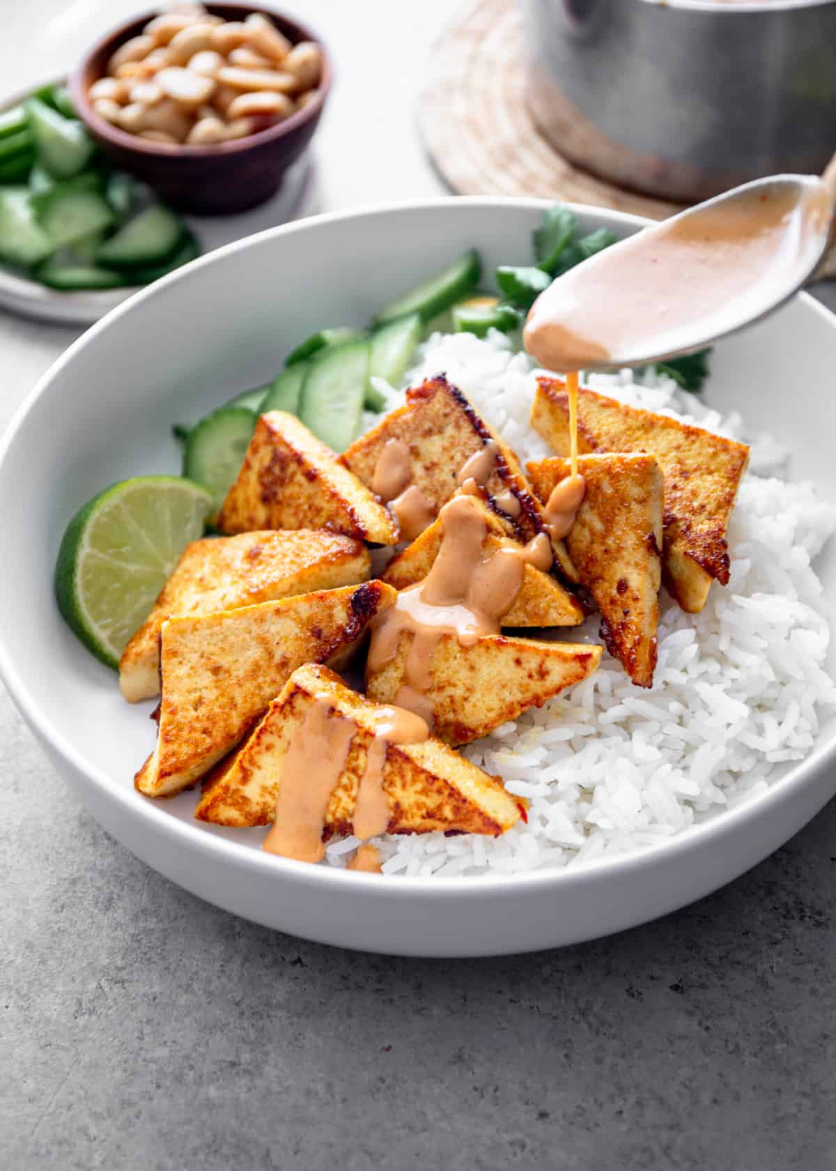 drizzling peanut sauce over tofu in a white bowl