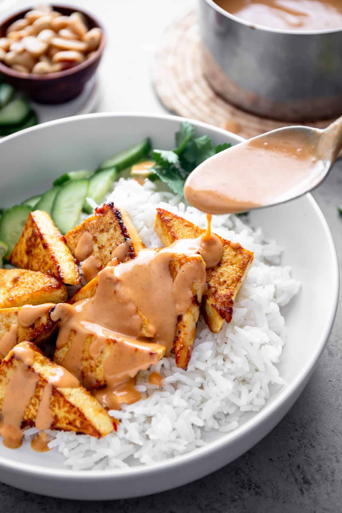 adding peanut sauce to tofu and rice in a white bowl