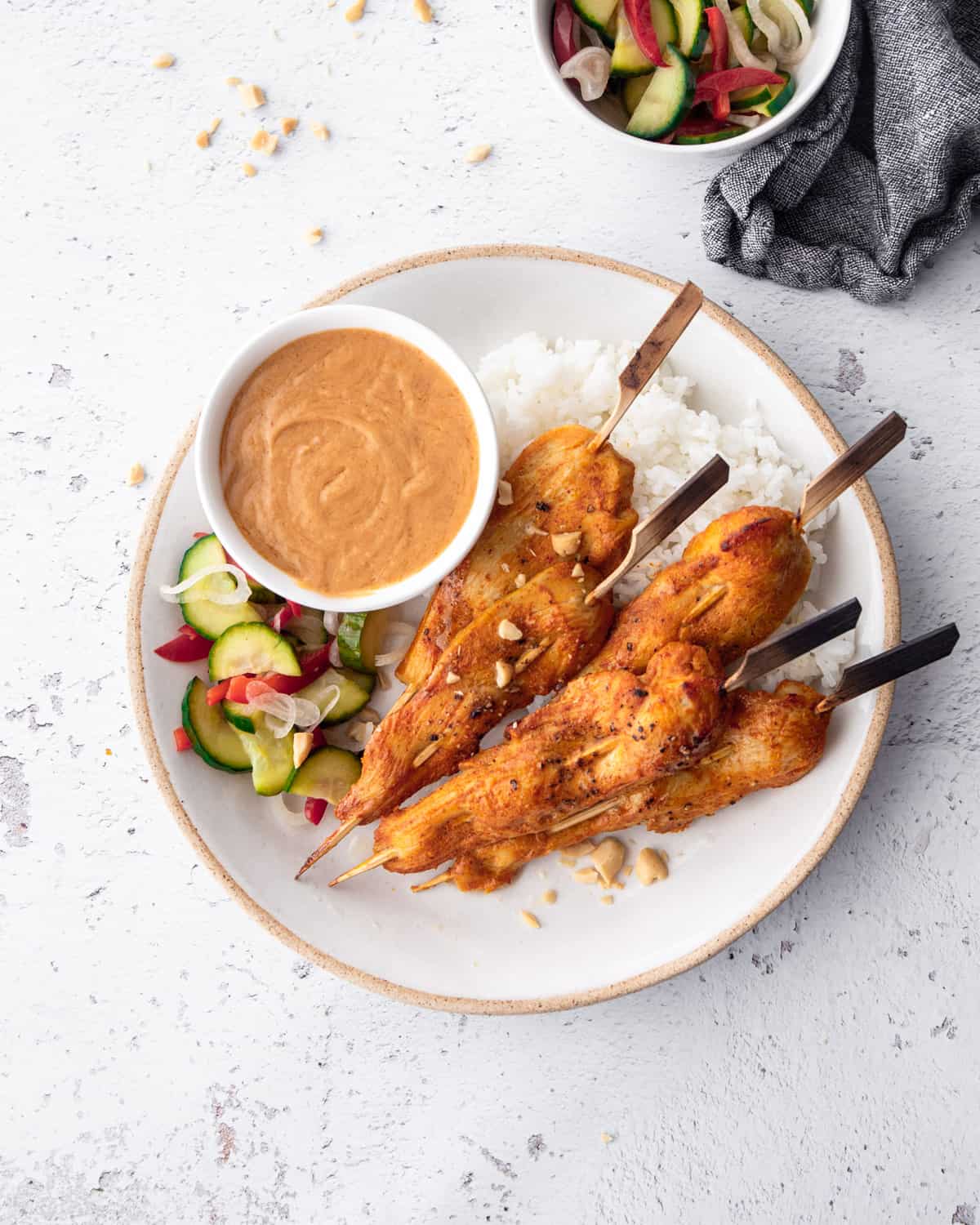 chicken satay, rice, pickles and peanut sauce on a white plate