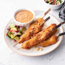 chicken skewers and peanut sauce on a white plate