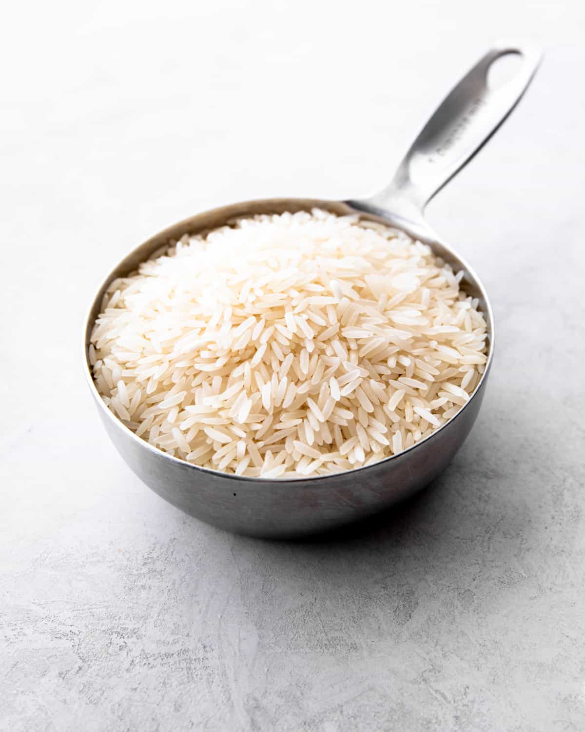 a measuring cup full of raw rice on a grey countertop