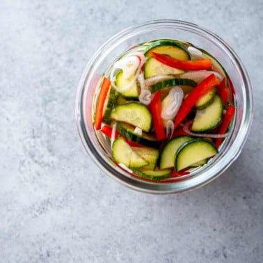 a glass jar of pickles on a grey countertop