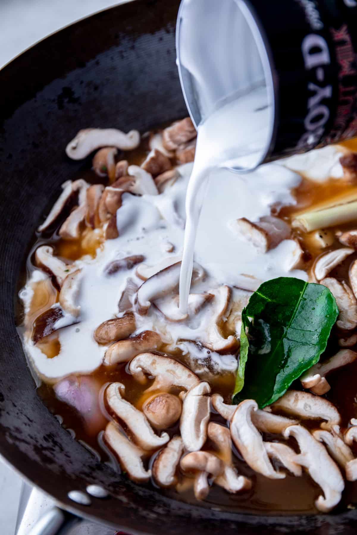 adding coconut milk to vegetables in a wok