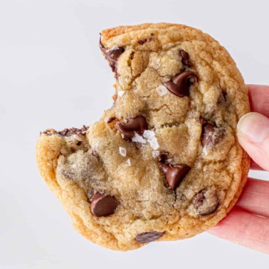 hand holding a chocolate chip cookie with a bite out of it