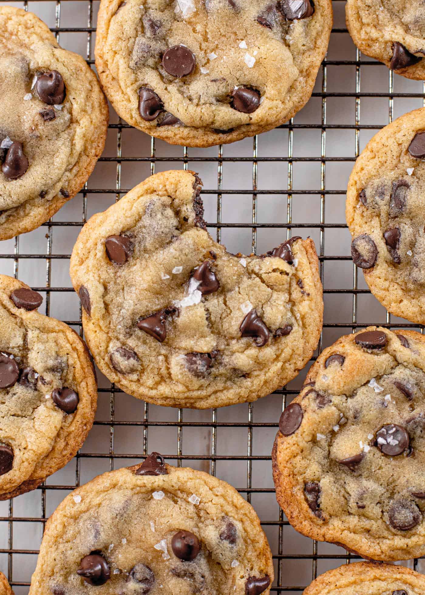 overhead image of chocolate chip cookies on a cooling rack with a bite out of the center cookie
