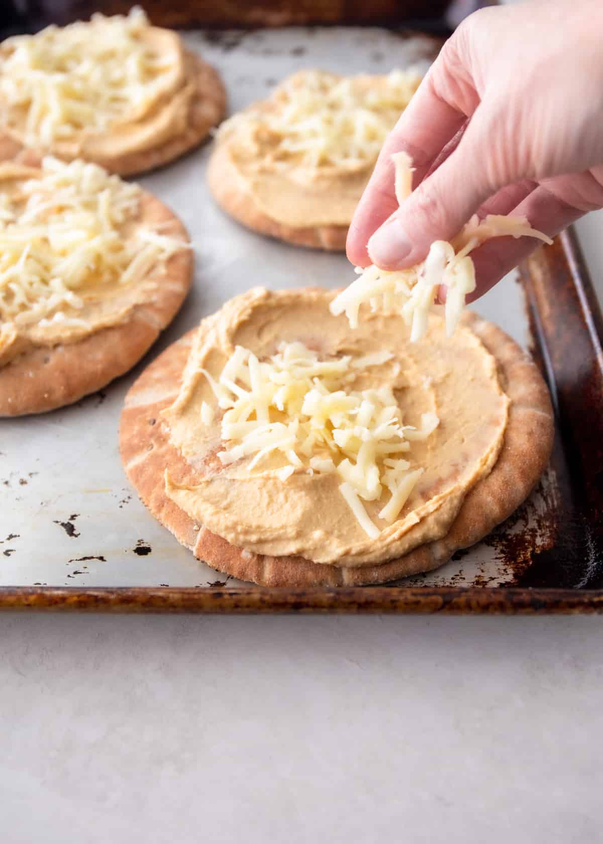 adding cheese to the top of flatbreads on a sheet pan