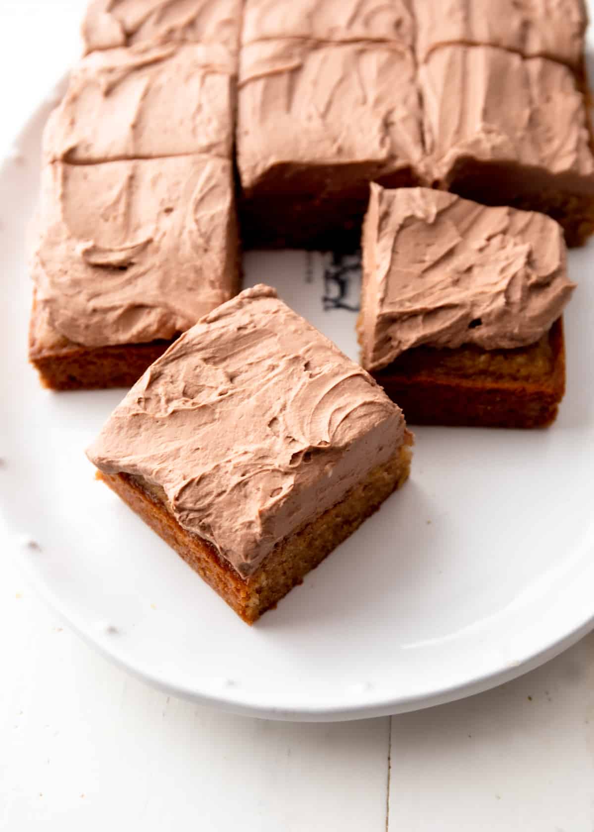 a square cake with chocolate frosting cut into square slices on a white plate