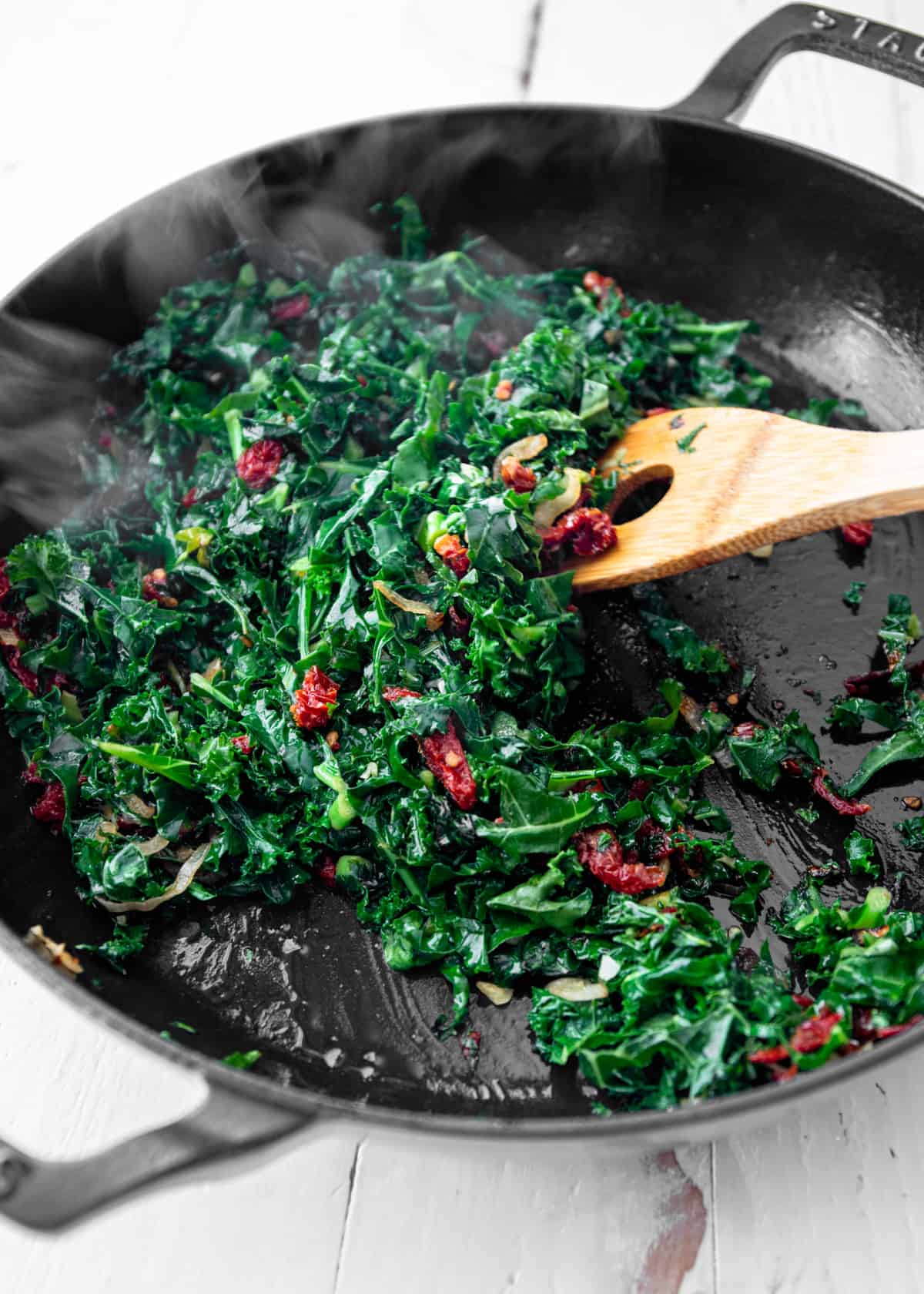 stirring kale and sun dried tomatoes in a cast iron skillet
