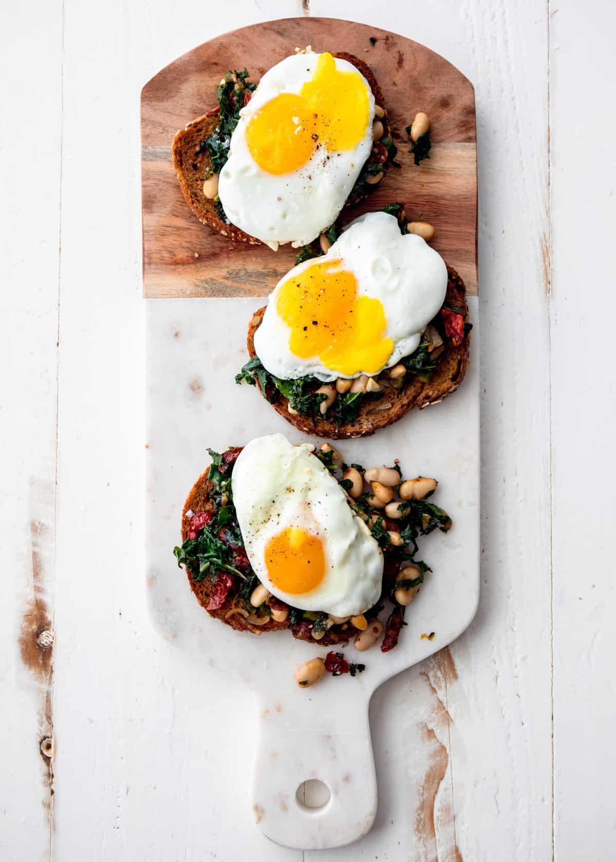 fried egg, white beans and kale on toasted bread on a cutting board