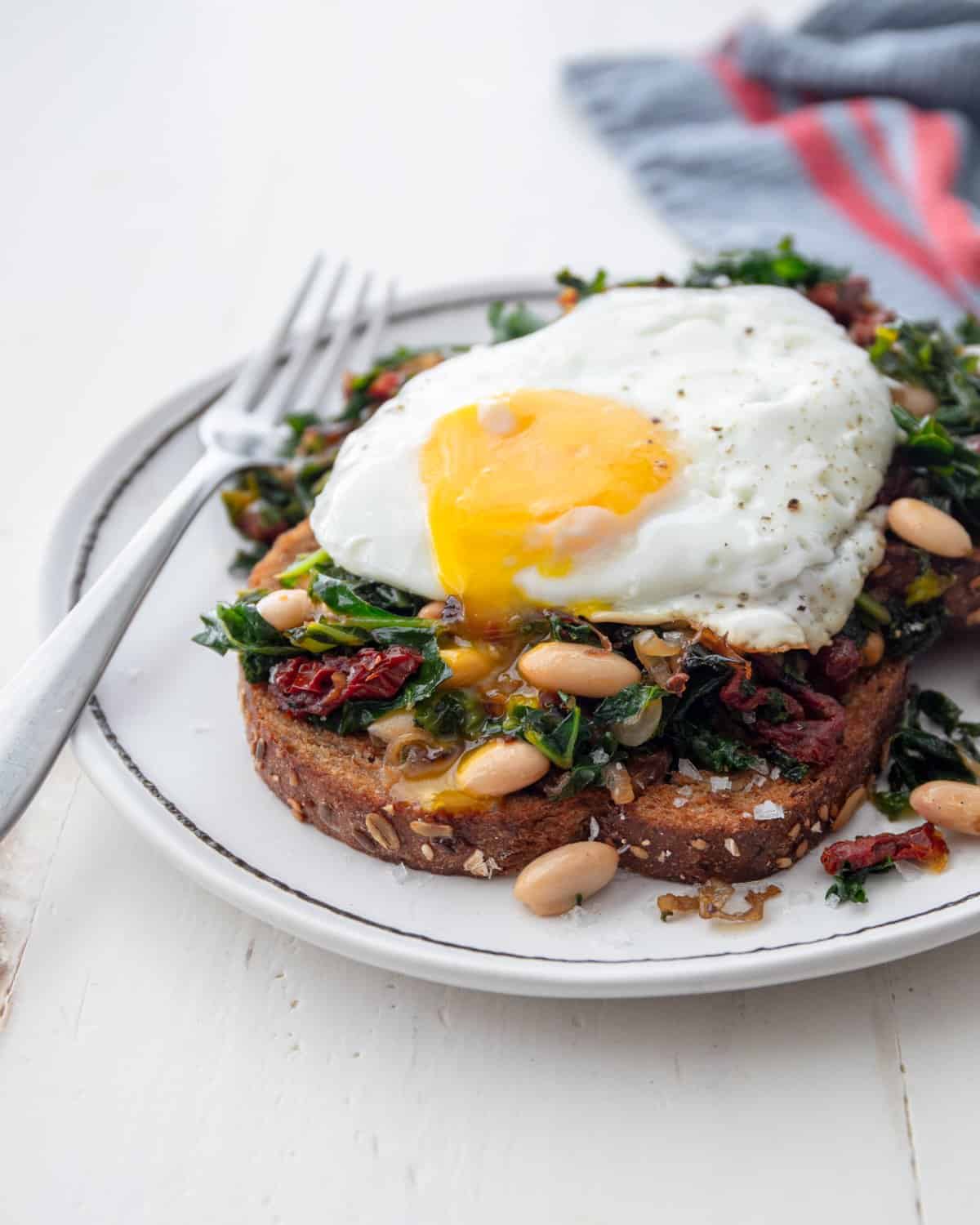 beans, kale and a fried egg on toast on a white plate