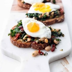 toasted bread topped with beans and greens on a cutting board