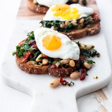 toasted bread topped with beans and greens on a cutting board