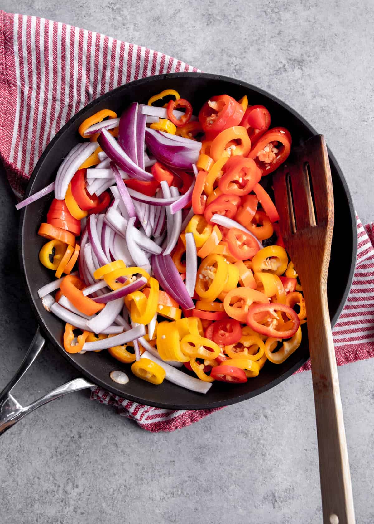 overhead image of a wooden spoon stirring sweet peppers and onions in a skillet