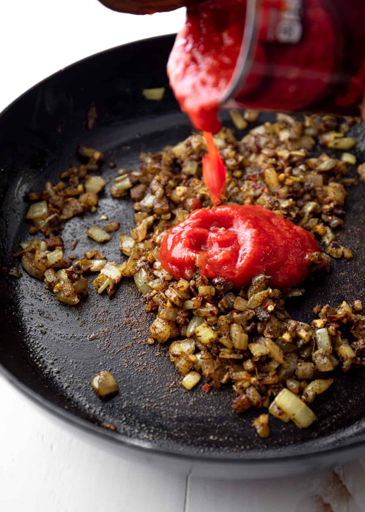 adding tomato sauce to vegetables in a cast iron skillet