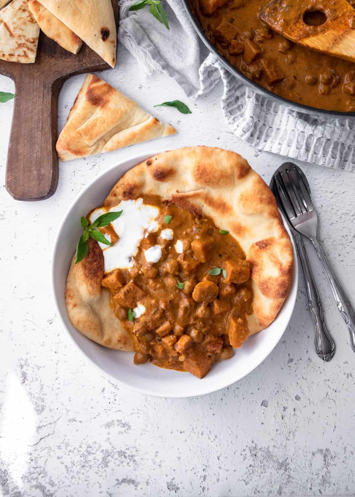 overhead image of curry and naan in a white bowl