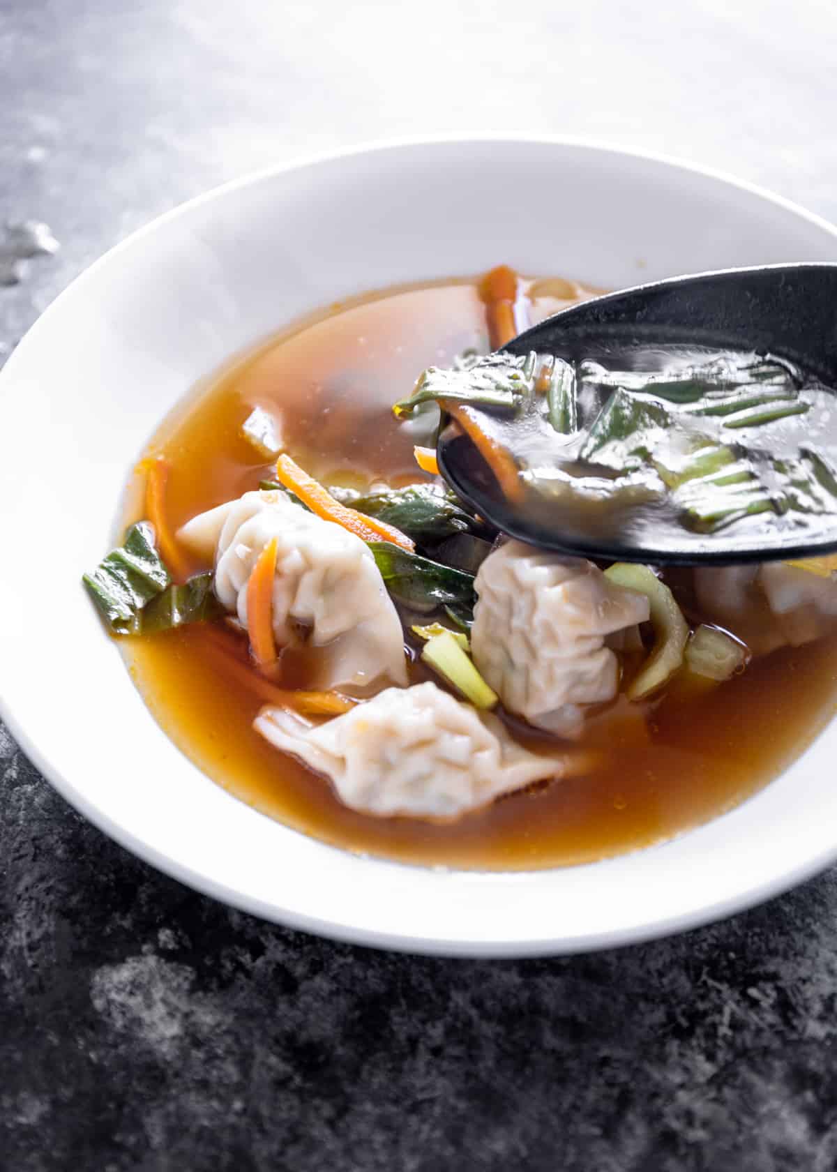 soup with wontons and vegetables in a white bowl