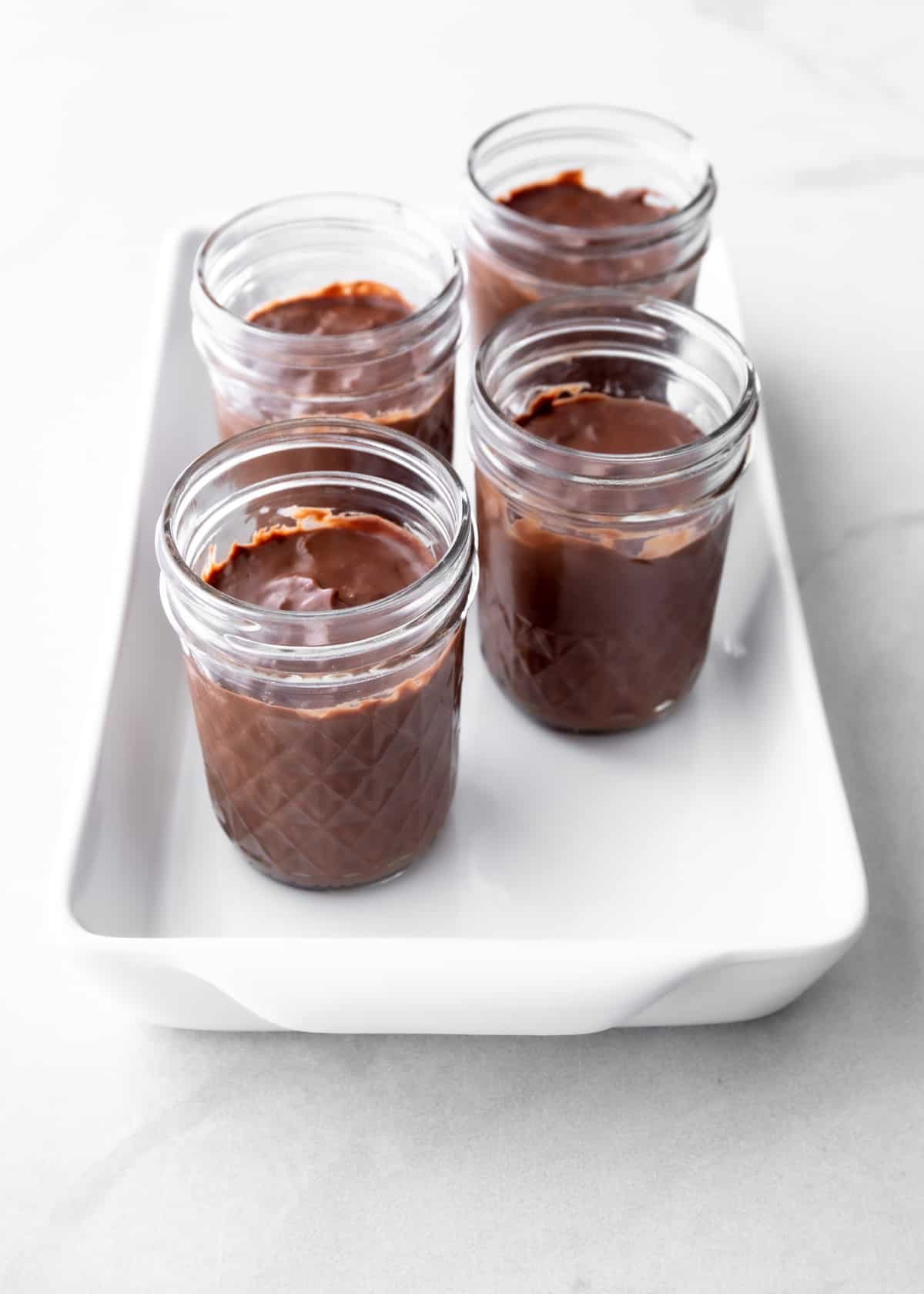 chocolate pudding in small glass jars in a white baking dish