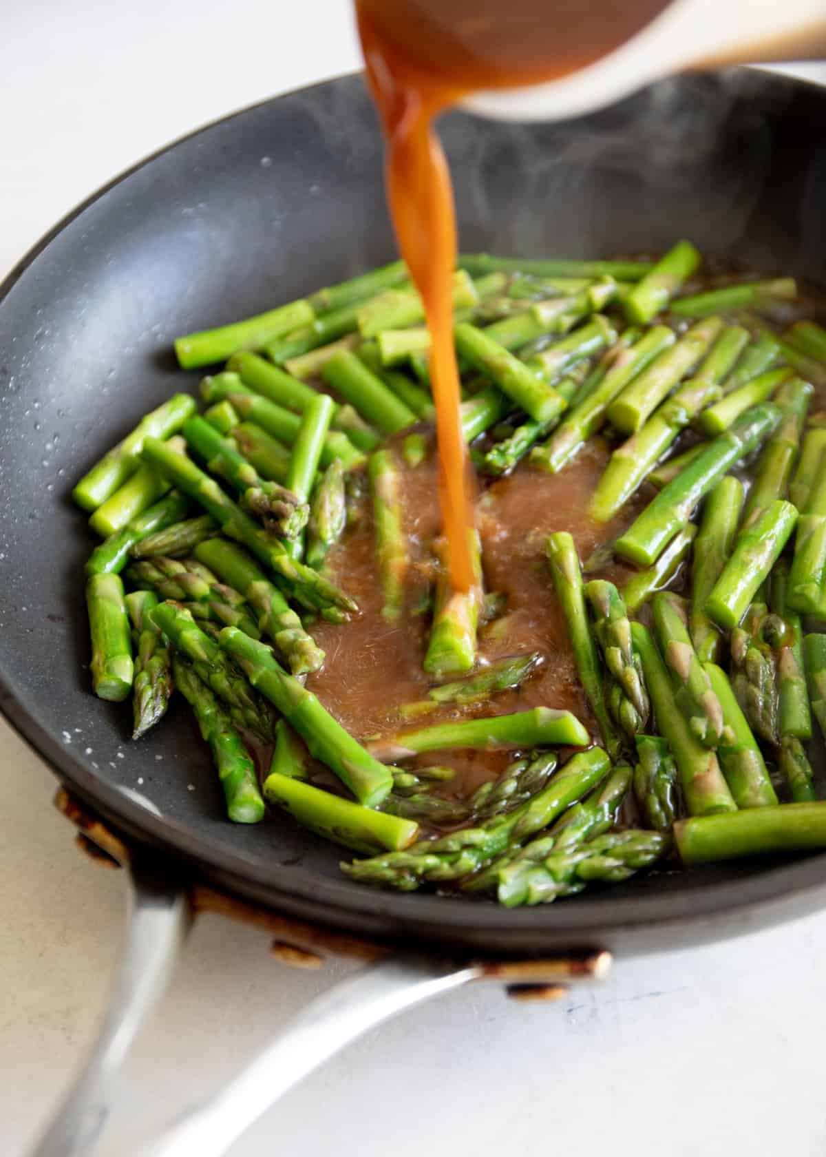 adding stir fry sauce to asparagus in a skillet