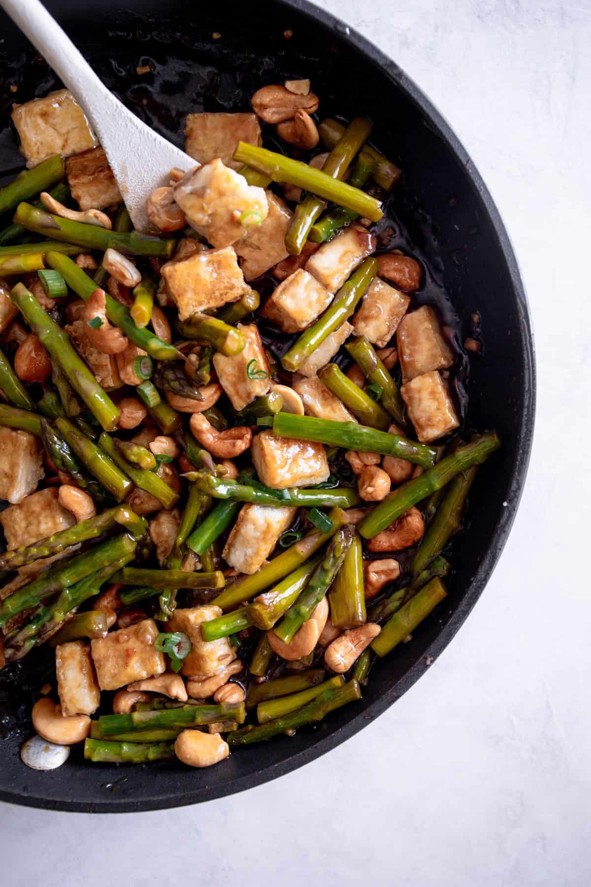 stirring cashews, asparagus, and tofu in a skillet